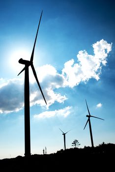 Wind turbine in the back light of the sun with blue sky and clouds.