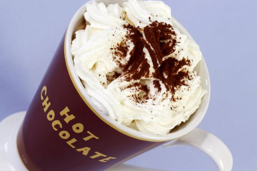A mug of hot chocolate with whipped cream over light blue background