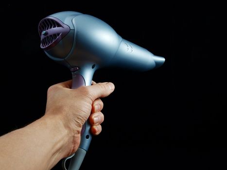 Silver colored hairdryer held by hand, towards black 