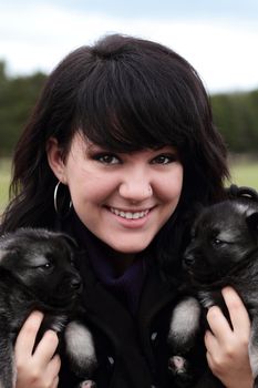 Attractive young woman holds two adorable purebred Norweigan Elkhound puppies.