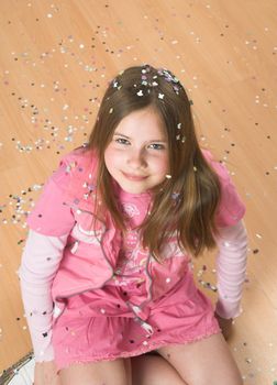 Little blond girl sitting on the floor covered in confetti