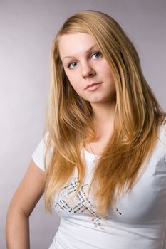 A smiling blonde on a grey background in studio.