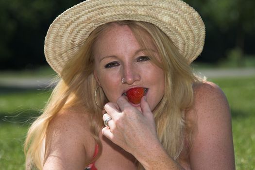 Beautiful blond woman with straw hat eating a strawberry