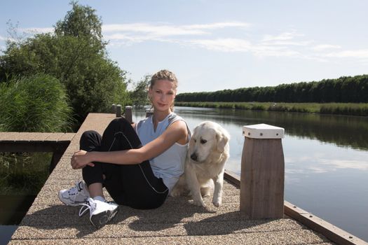 Pretty blond woman relaxing with her dog by the waterside