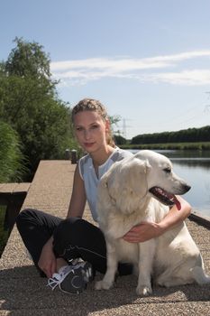 Pretty blond woman relaxing with her dog by the waterside