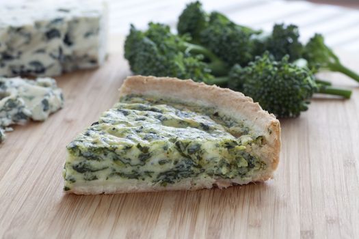 Slice of blue cheese and broccoli quiche with ingredients in background