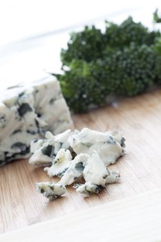 Crumbled blue cheese with block of cheese and broccoli in background.