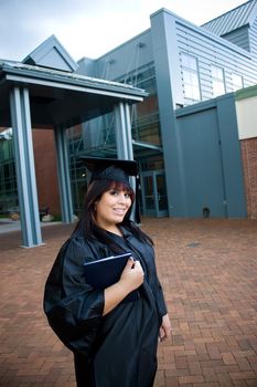 A recent graduate posing outdoors with her diploma tucked in her arm.