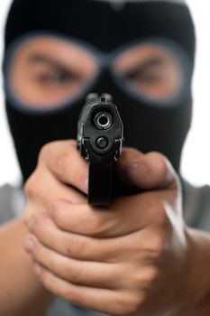 An angry looking man wearing a ski mask pointing a black handgun at the viewer. Works great for crime or home security concepts.