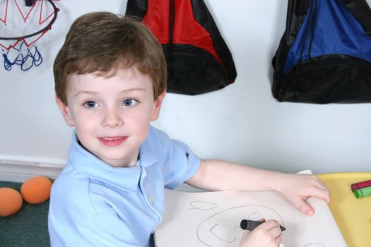 Handsome and happy little boy sitting at a pre-school table coloring with jumbo crayons.  Shot with the Canon 20D.