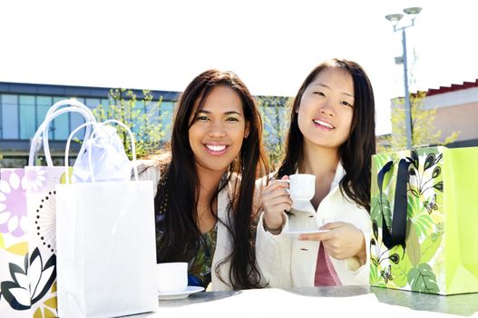 Two girl friends sitting and having drinks at outdoor mall with shopping bags