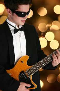 Attractive young man teenager  in tux with electric guitar over defocused lights.