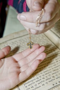 Hands close up with an orthodox cross against the orthodox bible 