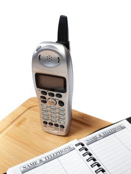 A cordless phone on a cutting board, with a blank name and telephone directory, isolated on white.