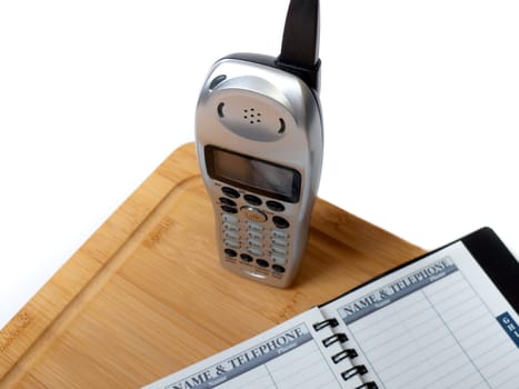 A cordless phone on a cutting board, with a blank name and telephone directory, isolated on white.