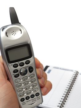 A hand holding a cordless phone, with the display facing the camera, and a blurred blank telephone directory in the background, isolated on white.