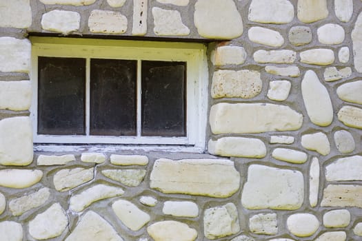 A dirty window surrounded by a shore stone wall.