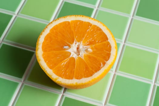 Half of the juicy orange on green tiled bar