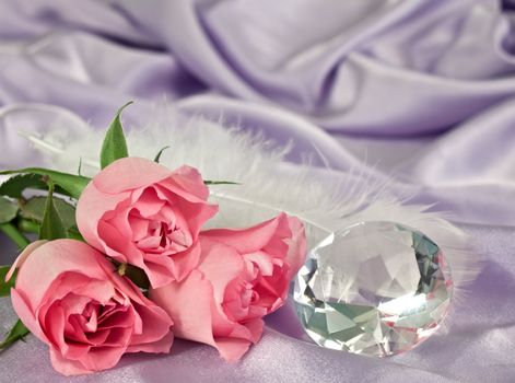 Three pink rosebuds and a diamond lying on lilac satin