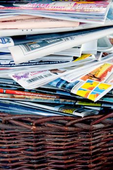 A stack of magazines and newspaper in a brown basket
