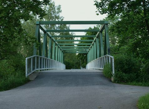 pedestrian bike path leading to a metal bridge covered with green trees