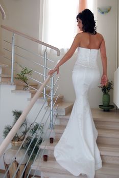 Rear view of young bride wearing white dress walking up staircase.