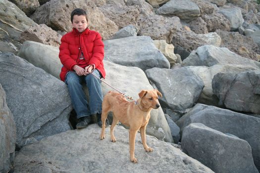 Young boy sitting on natural rock background with his licensed puppy