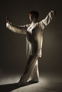 young woman in white suit make's taiji chuan exercise in studio