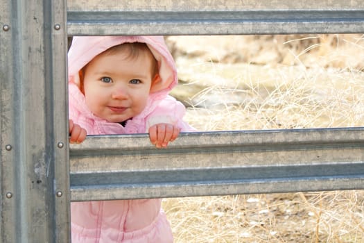 A cute girl peeking through a gate.