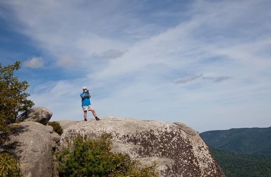 Male hiker looks over valley in the Shenandoah on a climb of Old Rag and takes a photo