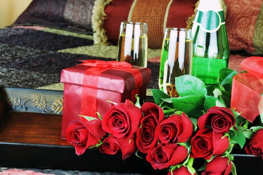 Flowers and wine on a breakfast tray sitting on a bed.