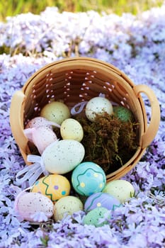 Easter eggs spilling from a basket into a bed of spring flowers. Selective focus on center portion of image where eggs are spilling out with extreme shallow DOF. Some blur on lower portion.