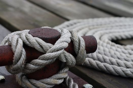 A closeup of a cleat on the dock, with a rope tied around it.