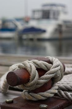 A closeup of a cleat on the dock, with a rope tied around it.