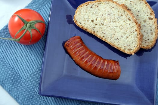 Sausage on blue plate with bread and red tomato