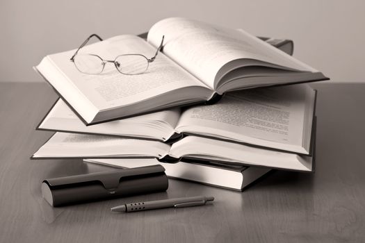 opened books pen and glasses on sepia background