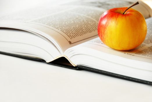 large opened book with ripe red yellow apple