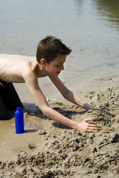 Boy having fun with sand on the waterside.