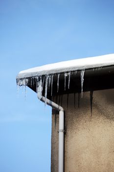small icicles hanging from the eaves of a house against a blue sky with space for text
