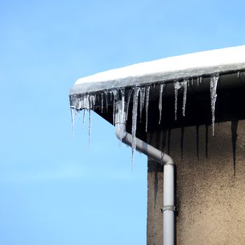 Danger - small icicles hanging from the gutter in front of blue sky
 