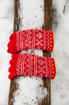 A pair of red wool mittens lying on a snow covered log