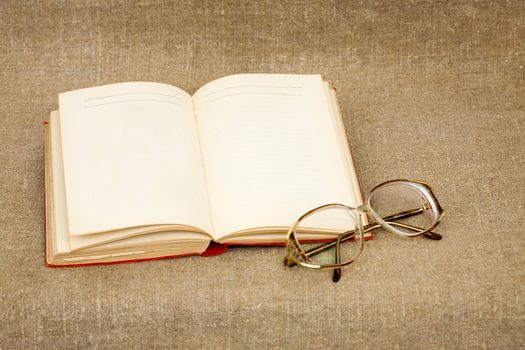Ancient book and spectacles on the fabric background