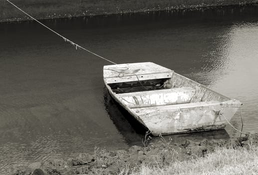 Old boat along the shore in very poor condition shown in black and white