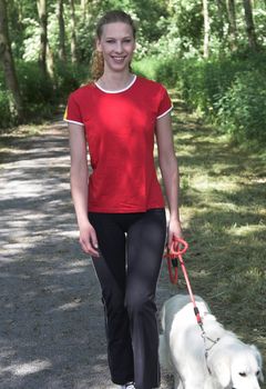 Pretty blond woman walking in the woods with her dog