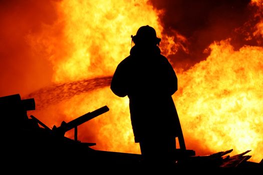 Fireman fighting a raging fire with huge flames of burning timber