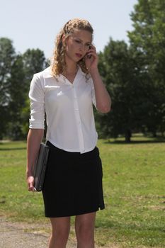 Pretty blond businesswoman talking on the phone while on her lunchbreak in the park