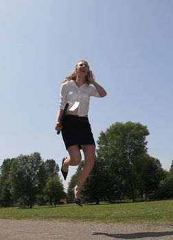 Businesswoman jumping in happiness with laptop under her arm and while still on the phone