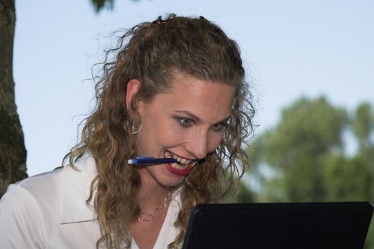 Beautiful businesswoman starting to go slowly crazy while looking at her laptop, with a pencil in her mouth