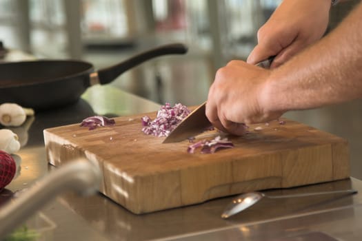 Man cutting the onions on a wooden board (shallow dof, some movement in the hands due to cutting)