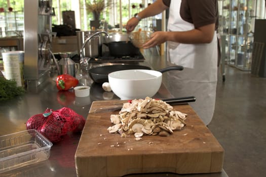 View of a kitchen with someone cooking in the background (focus on mushrooms in foreground, shallow dof)